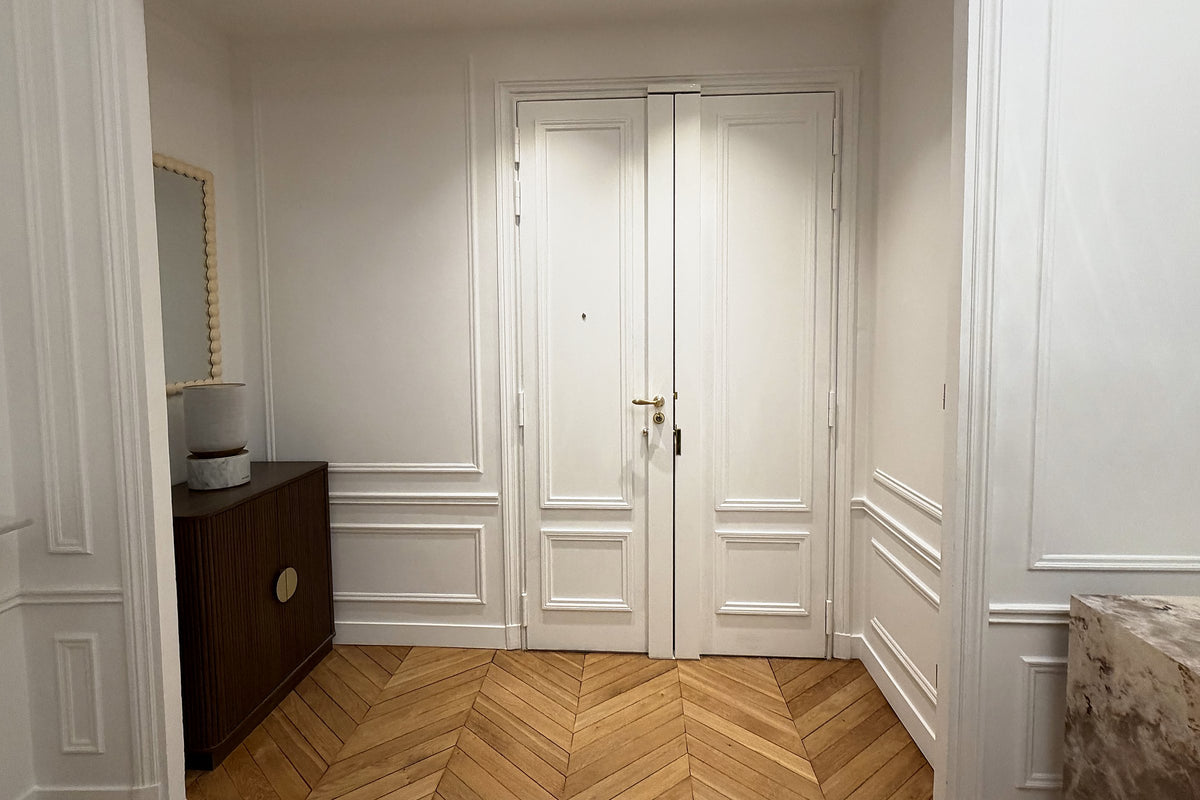 Entrée d’appartement haussmannien à Paris : parquet en point de Hongrie et double porte blindée moulurée blanche
