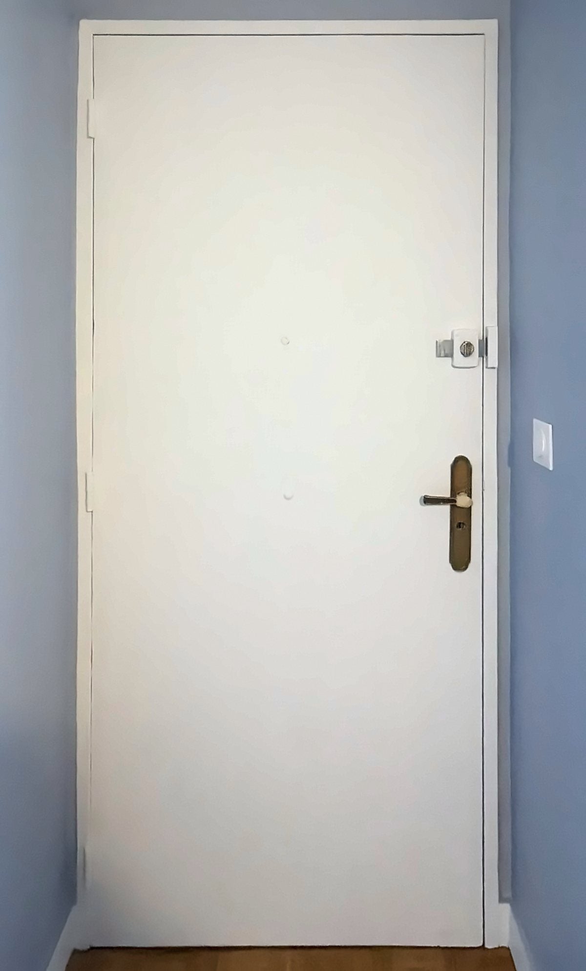 Porte d’entrée d’appartement à Paris avant blindage : porte blanche, verrou en applique et béquille en laiton